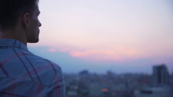 Guy olhando para o horizonte rosa da paisagem da cidade, pensando sobre a vida, liberdade — Vídeo de Stock