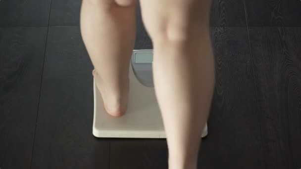 Женщина наступает на весы, слово слишком много появляется на экране, избыточный вес, сзади — стоковое видео