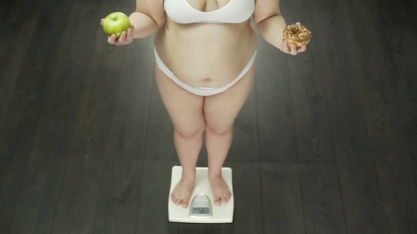 Healthy dieting lady standing on scales, holding apple and donut, choosing fruit — Stock Video