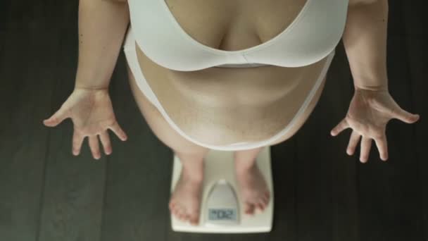 Παχύσαρκη γυναίκα στέκεται στις κλίμακες χέρια απεγνωσμένα χειρονομώ, λίπος στην κοιλιά, το top view — Αρχείο Βίντεο