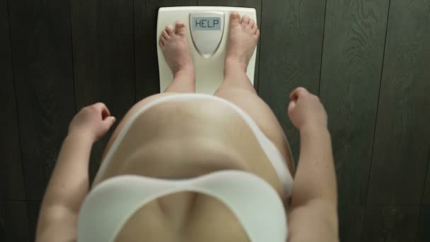 Femme obèse avec un poids supplémentaire debout sur les échelles avec aide de mot à l'écran, graisse — Video