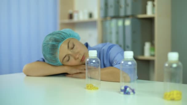 Overworked nurse sleeping on table, waking up and leaving with pill bottles — Stock Video