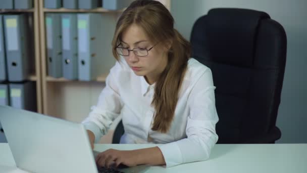 Жінка в білій сорочці працює за комп'ютером, друкуючи і уважно дивлячись на екран — стокове відео