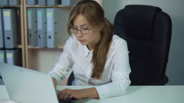 Женщина в белой рубашке работает за компьютером, печатает и внимательно смотрит на экран — стоковое видео