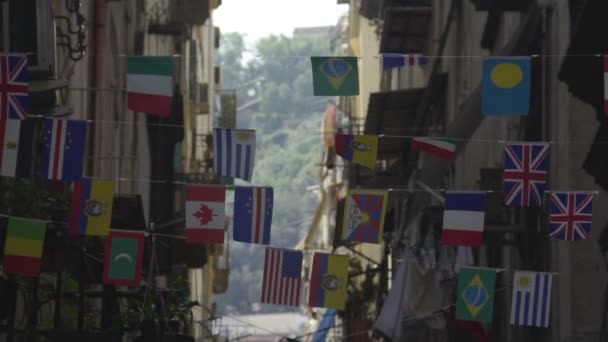 Banderas de diferentes países colgando de cuerdas entre edificios, balanceándose en el viento — Vídeos de Stock