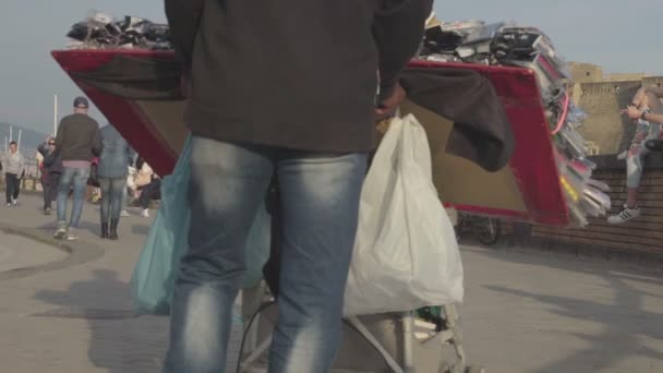 НАПЛЕС, ИТАЛИЯ - CIRCA JULY 2014: Люди в городе. Мужчина продаёт сувениры для туристов на улице приморского города, люди прогуливаются — стоковое видео
