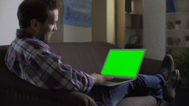 Adam kanepede oturan ve Web sitesinde sosyalleşme yeşil ekranlı dizüstü bilgisayar kullanarak