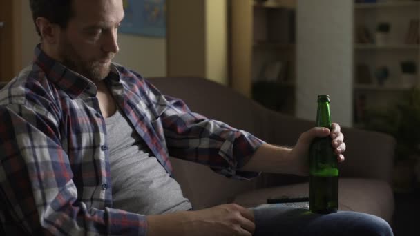 Потраченный парень, сидящий на диване, пьющий пиво, алкоголизм, психологические проблемы — стоковое видео
