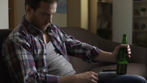 Мужчина дремлет на диване с бутылкой пива в руке, имея пьяные икоты — стоковое видео