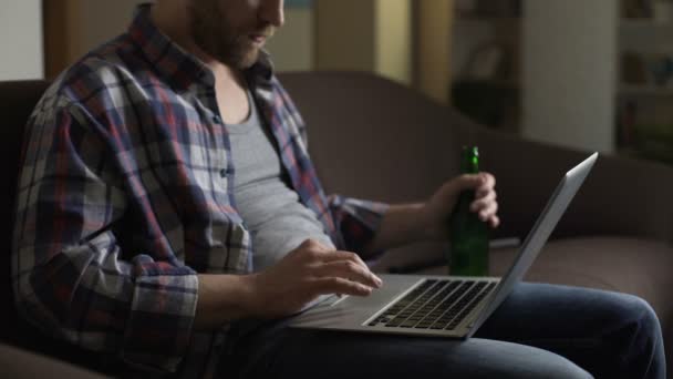 Slordig man op de Bank met behulp van de laptop en het drinken van bier, surfen internet, eenzaamheid — Stockvideo