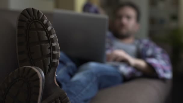 Ragazzo sdraiato sul divano e che utilizza laptop, siti web sociali, comunicazione con gli amici — Video Stock