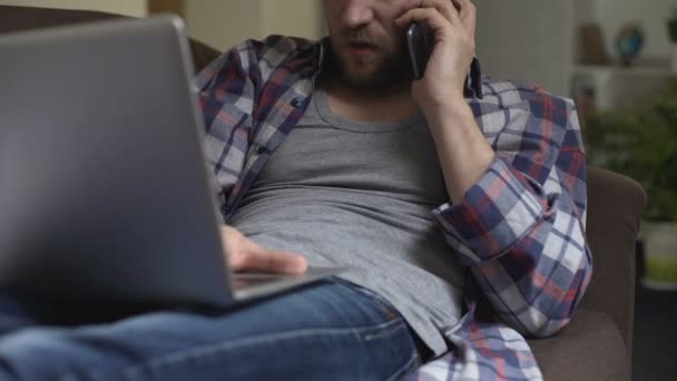 Hombre molesto tener conversación a través del teléfono móvil y el uso de la computadora portátil, negativo — Vídeo de stock