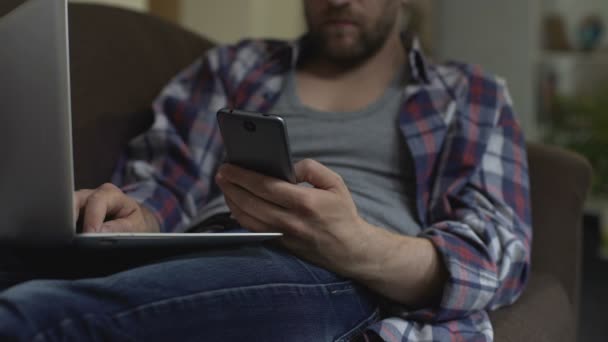 Взрослый мужчина с помощью приложения телефона, ноутбук на коленях, онлайн оплата, подтверждение — стоковое видео