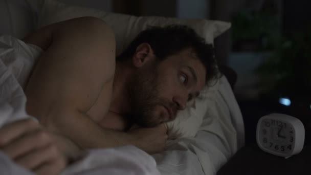 Хлопець повороту в ліжку не в змозі заснути, дивлячись сердито годинник, безсоння — стокове відео