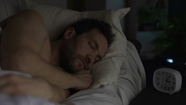 Hombre barbudo durmiendo en el sofá cama, reloj de pie en la mesa de noche, descanso nocturno — Vídeos de Stock