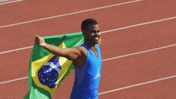 Bandera de Brasil ondeando en el viento, atleta mostrando su fuerza, ganando la competencia — Vídeos de Stock