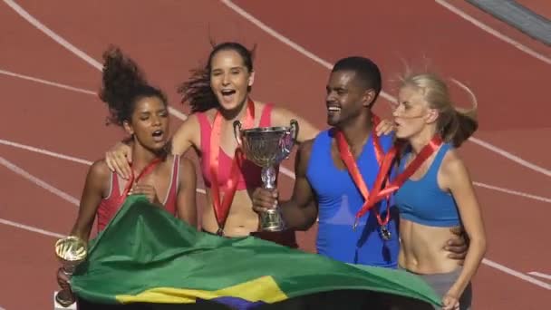 Atletas felices saltando con bandera brasileña regocijando victoria, competición deportiva — Vídeo de stock