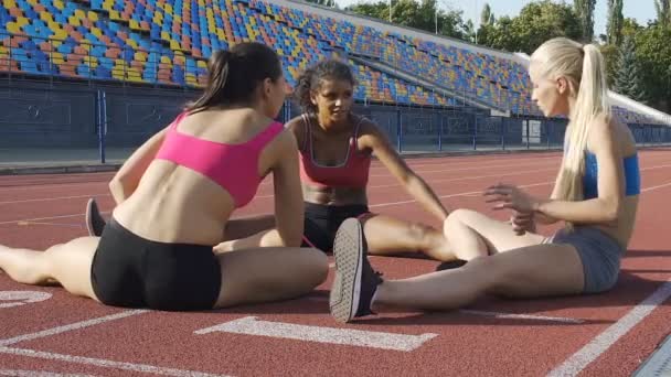 Tres chicas atletas sentadas en el campo de deportes y estiramiento, entrenamiento y fitness — Vídeos de Stock