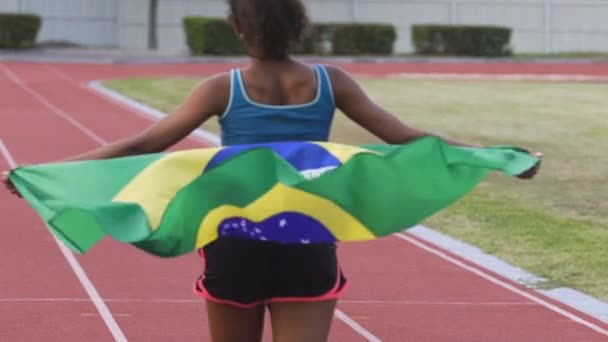 Junger zweirassiger Sieger eines Sportwettbewerbs, der auf einer Arena mit brasilianischer Flagge läuft — Stockvideo