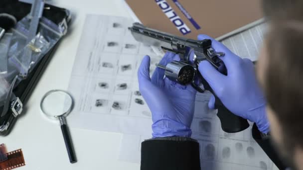 Police officer checking revolver with magnifier, evidence from suicide scene — Stock Video