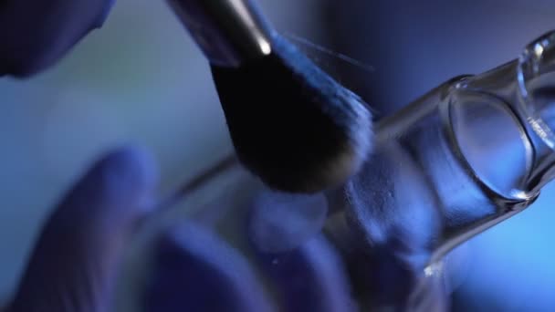 Plan rapproché de la révélation de l'empreinte latente de la bouteille, à l'aide d'un pinceau et de poudre 