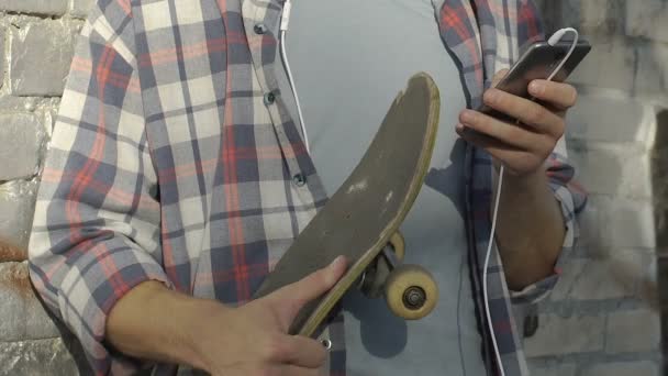 Young male skater listening to music in smartphone, chatting friends, student — Stock Video