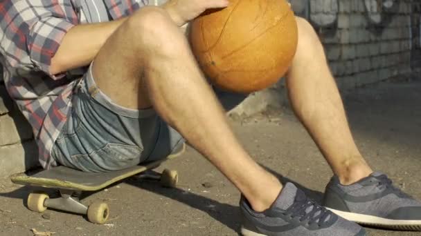 Мальчик-подросток в повседневной одежде сидит на скейтборде, активно проводит время — стоковое видео