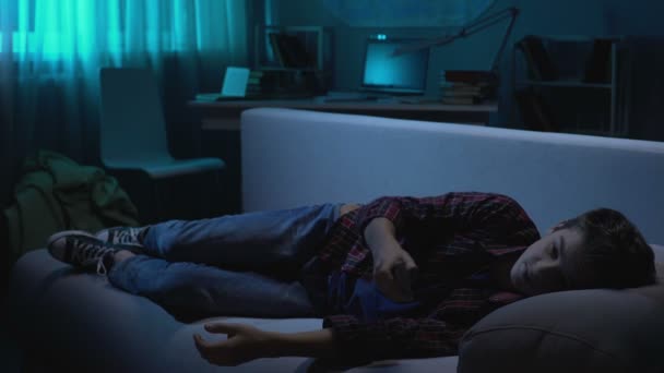 Підліток розслабляється на дивані і засинає перед телевізором, вільний час вдома — стокове відео