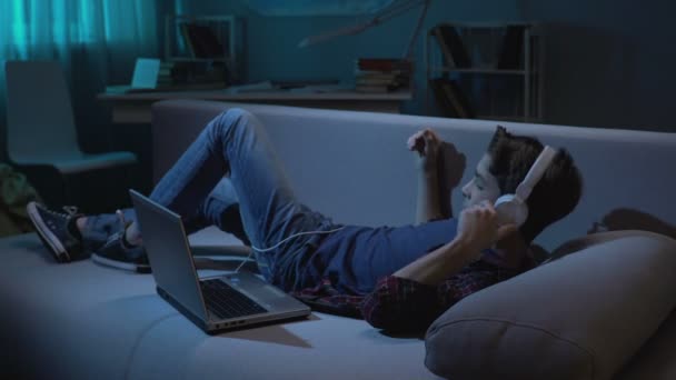 Mand teenager i headset hviler på sofaen, ser sig omkring og ser voksent indhold – Stock-video