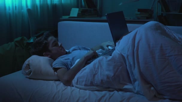 젊은이 그의 침대에 누워 하 고 밤 시간에 노트북 컴퓨터 게임 — 비디오