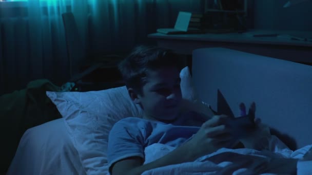 Мужчина студент играет в игры на смартфоне в постели ночью, гаджет наркомании — стоковое видео
