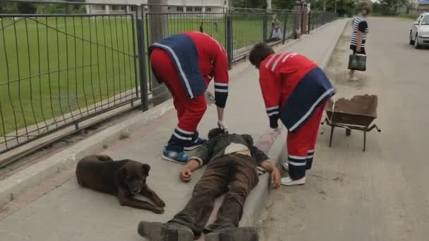 Ambulanspersonal försöker undersöka full hemlös man liggande på gatan — Stockvideo