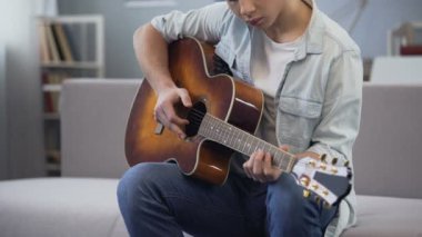 Erkek genç onun odasında oturup gitar çalmayı öğrenme müzik pratik