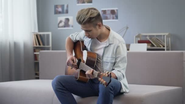 Adolescent garçon avec enthousiasme tuning guitare assis dans son chambre, passe-temps de la musique — Video