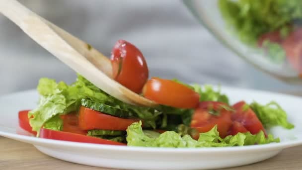 Женщина кладет свежий овощной салат из миски в тарелку, здоровую закуску, детоксикацию — стоковое видео