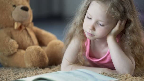 Солодка маленька дівчинка поглинута казкою, читаючи улюблену книгу з інтересом — стокове відео
