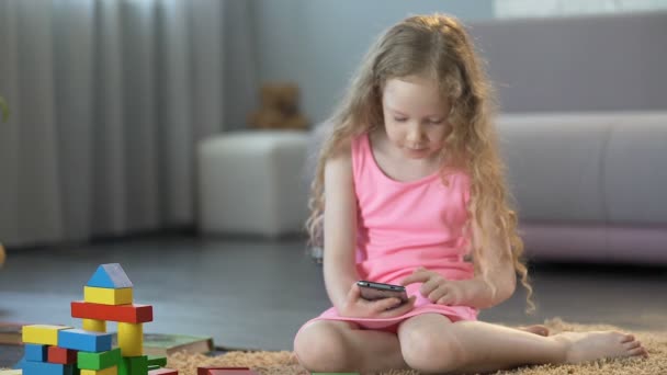 Niña ignorando los juguetes, jugando juegos en la aplicación móvil, adicto al teléfono inteligente — Vídeo de stock