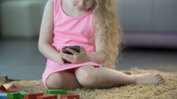 Zajęty małej dziewczynki za pomocą gadżetu na komórke, grając w gry na smartfonie, technologia — Wideo stockowe