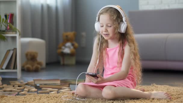 Little kid listening to favorite music on gadget and singing song in headphones — Stock Video