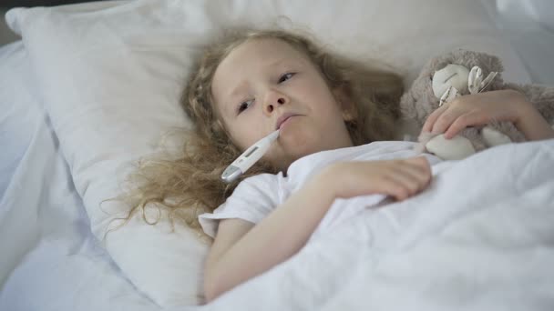 Sjuka lilla flickan liggande i sängen sorgligt med termometer i munnen, kid fångat kallt — Stockvideo