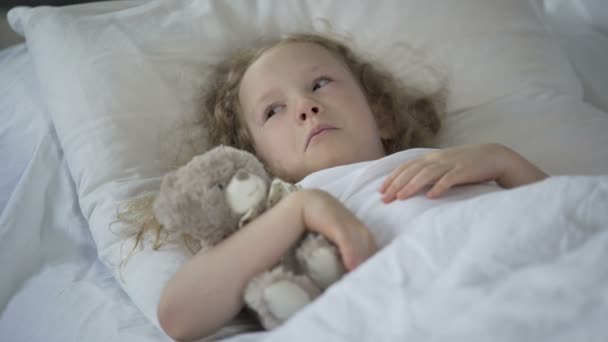 Сумна дівчинка з іграшкою плаче в ліжку, нещаслива хвора дитина почувається самотньою — стокове відео
