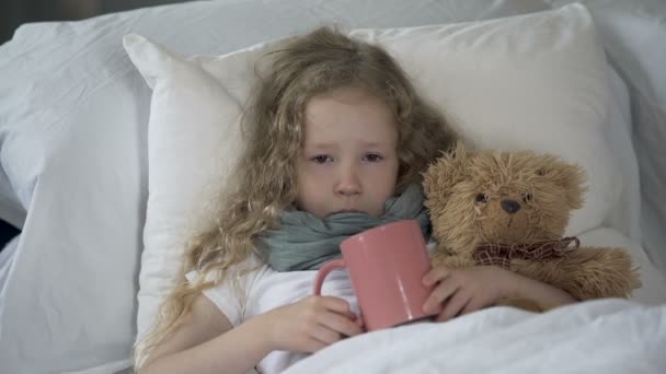 Δυστυχισμένος άρρωστο παιδί ξαπλωμένη στο κρεβάτι με φλιτζάνι ζεστό ρόφημα, κορίτσι υποφέρει γρίπης — Αρχείο Βίντεο