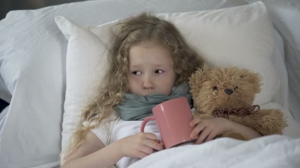 Criança doente deitada na cama com bebida quente na caneca, menina doente chorando de dor de garganta — Vídeo de Stock