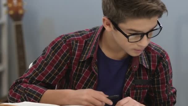 Intelligenter Teenager mit Brille, der Informationen in Büchern überprüft, Essays schreibt, Indigo — Stockvideo