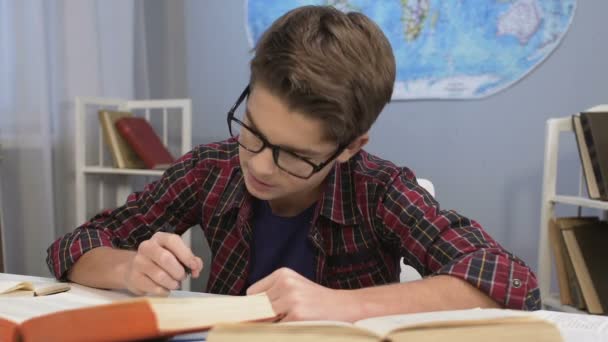 Genius boy in glasses doing homework task, writing answers in notebook, essay — Stock Video