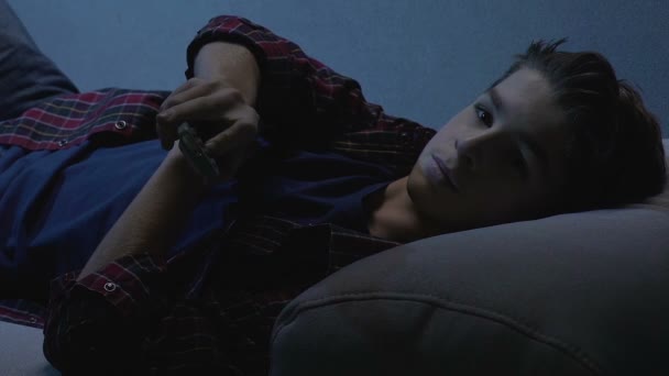 Έφηβος αγόρι ξαπλωμένος στον καναπέ και βλέποντας τηλεόραση νύχτα μόνος, αλλαγή καναλιών — Αρχείο Βίντεο