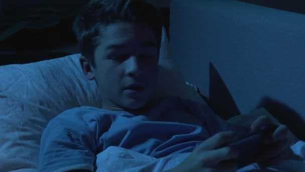 Мать берет телефон, пока сын играет в мобильную игру в постели ночью, наркомания — стоковое видео
