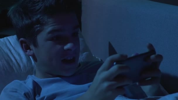 Adolescent irrité garçon jouer jeu mobile dans le lit temps de sommeil, perdre rond — Video