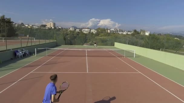 Молодой человек и женщина играют в теннис на спортивном курорте, панорамный вид на корт — стоковое видео