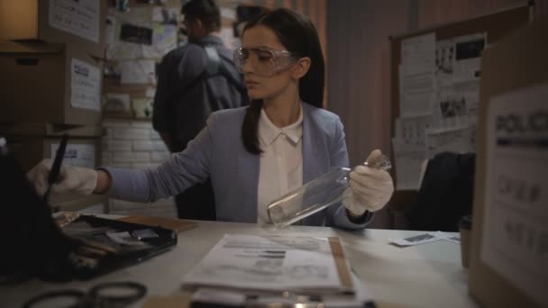 Oficial femenina calificada tomando las huellas dactilares de la botella de vidrio de evidencia — Vídeos de Stock